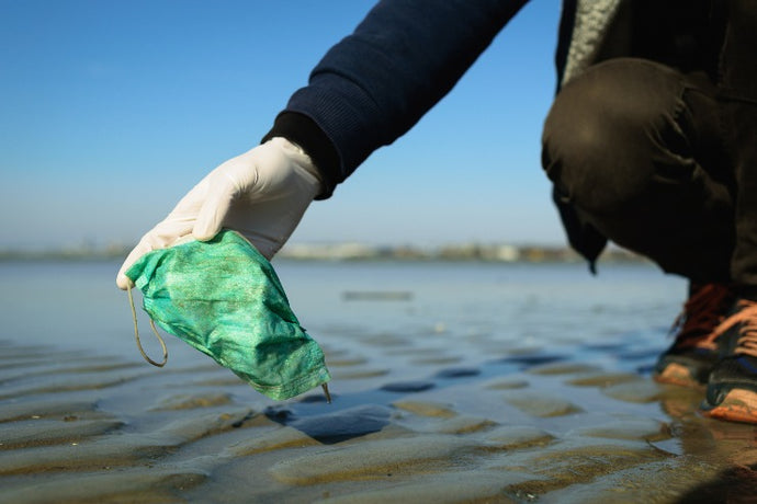 a person with gloves picks up a plastic face mask from a lake | Lumiere Paris